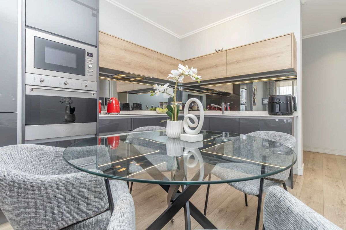 Modern kitchen featuring sleek laminate cabinetry, a mirrored splashback, integrated oven and microwave, and high-quality laminate flooring.