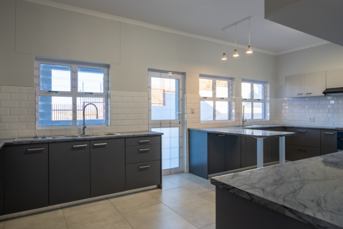 Modern kitchen featuring dark cabinetry, stone countertops, subway tile backsplash, and large format floor tiles with ample natural light.