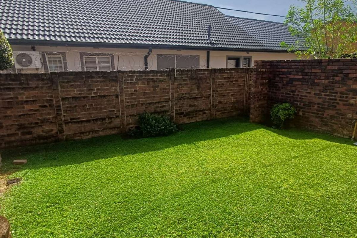 A private rear garden featuring a well-maintained lawn enclosed by a brick boundary wall with security razor wire.