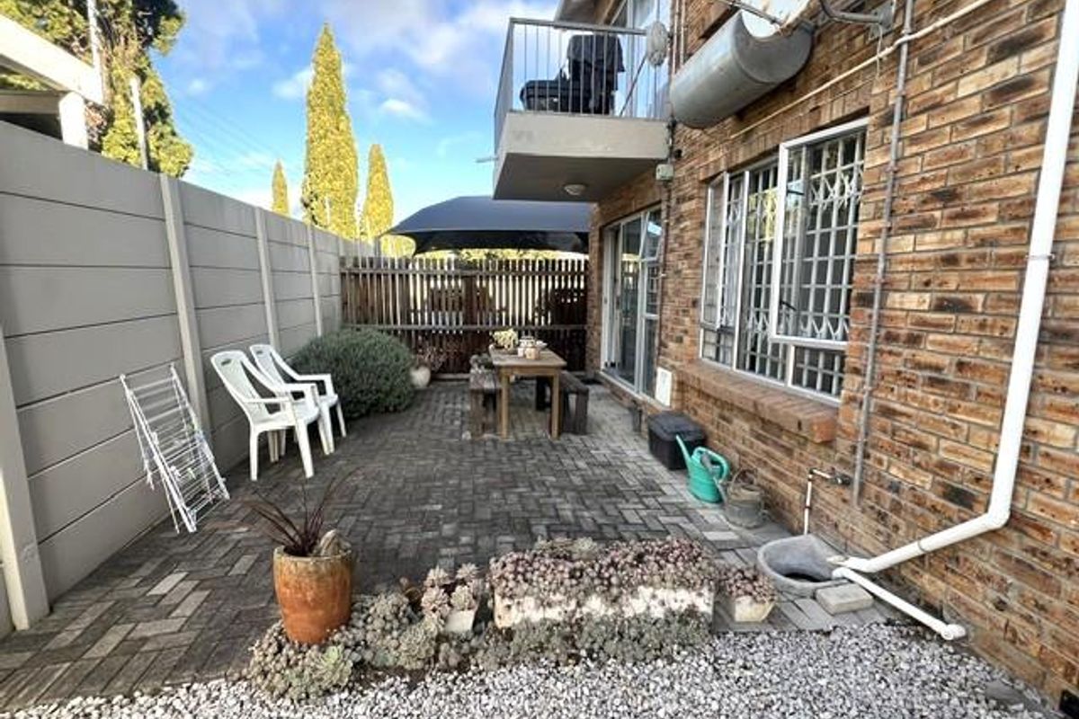 A private rear courtyard featuring brick paving, a precast boundary wall, and direct access to the apartment via a sliding door with security bars.