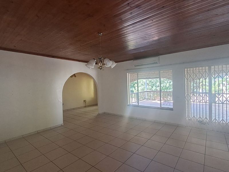 Spacious living area featuring tiled floors, a timber-clad ceiling, and an archway leading to an adjacent room, with direct access to an outdoor patio.