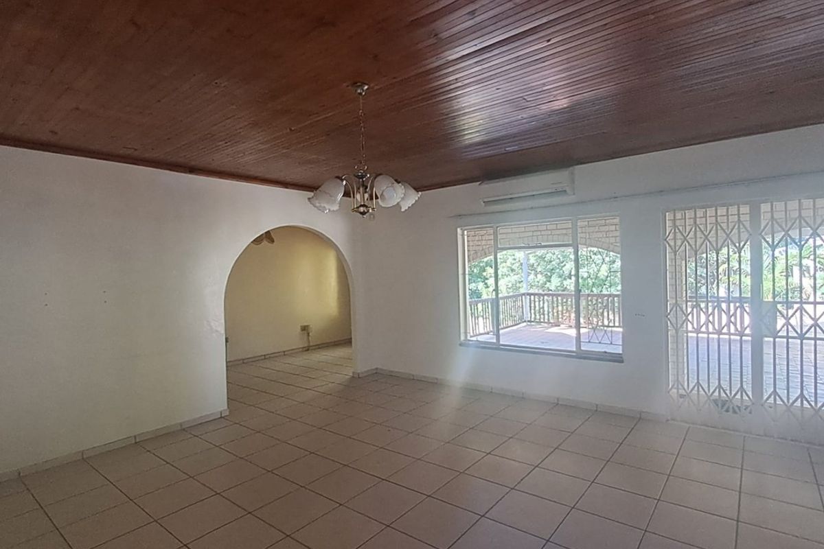 Spacious living area featuring tiled floors, a timber-clad ceiling, and an archway leading to an adjacent room, with direct access to an outdoor patio.