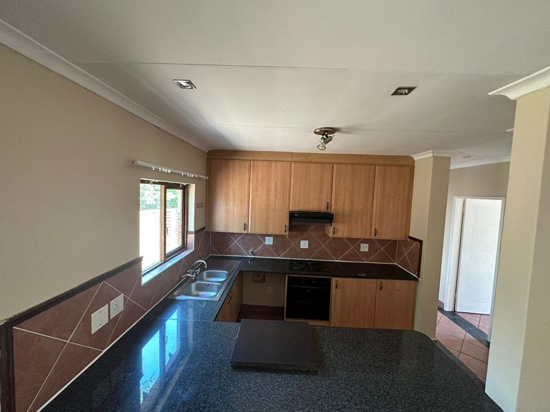 A functional kitchen featuring wooden cabinetry, granite countertops, a double basin sink, and built-in cooking appliances with a tiled backsplash.