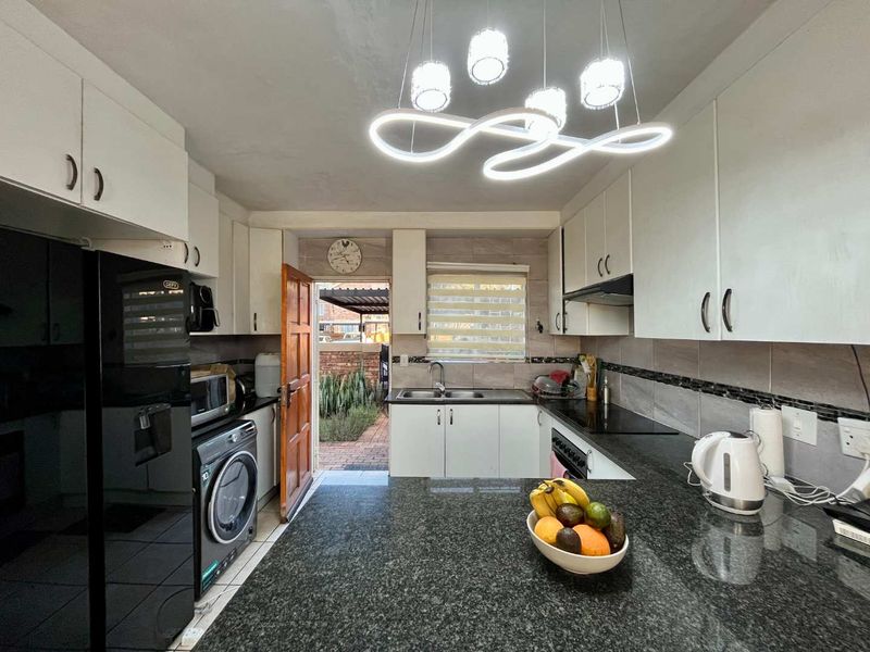 A functional kitchen featuring granite countertops, ample built-in cabinetry, a double basin sink, and a modern electric hob with an extractor fan.