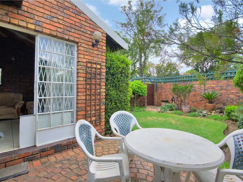 A private rear garden featuring a brick-paved patio area, established lawn, and perimeter brick boundary walls, accessible via a secure sliding door.