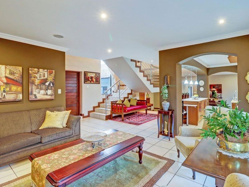 Spacious open-plan living area featuring tiled floors, a central staircase with metal balustrades, and a seamless transition into the kitchen space.