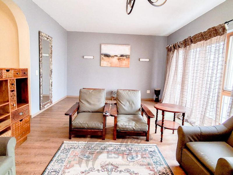 A living room featuring laminate flooring, an arched doorway, and wall-mounted lighting, offering a neutral base for interior design updates.