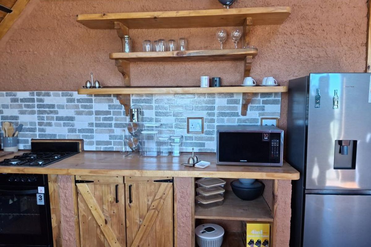 Rustic kitchen area featuring wooden cabinetry, open shelving, a brick-style tiled backsplash, built-in gas hob, and integrated microwave space.