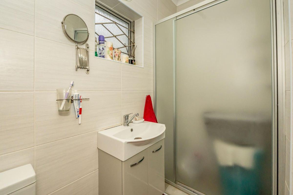 A compact bathroom featuring a modern vanity unit, a tiled shower enclosure with a frosted glass door, and a small window.
