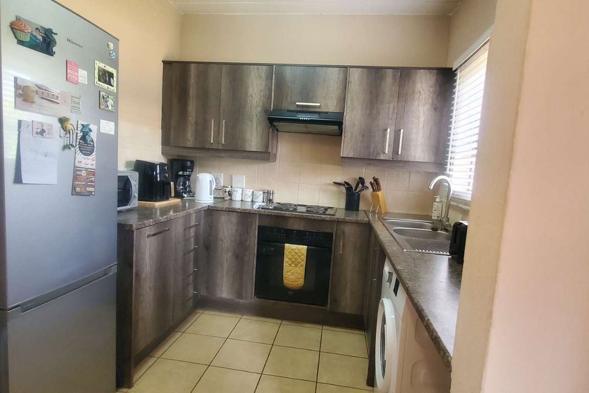 Compact kitchen featuring wood-look cabinetry, built-in oven, hob, extractor fan, and tiled flooring with integrated laundry plumbing.
