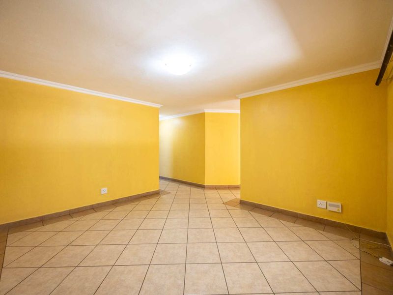 An empty, open-plan living area featuring neutral tiled flooring and bright yellow walls, offering a blank canvas for interior design.