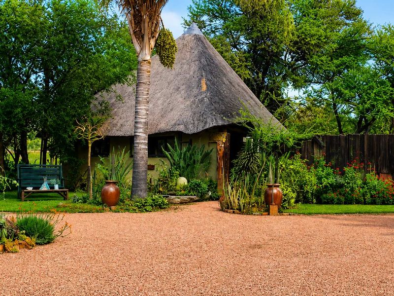 A charming farm-style cottage featuring a traditional thatch roof, surrounded by a lush, well-maintained garden and a spacious gravel driveway.