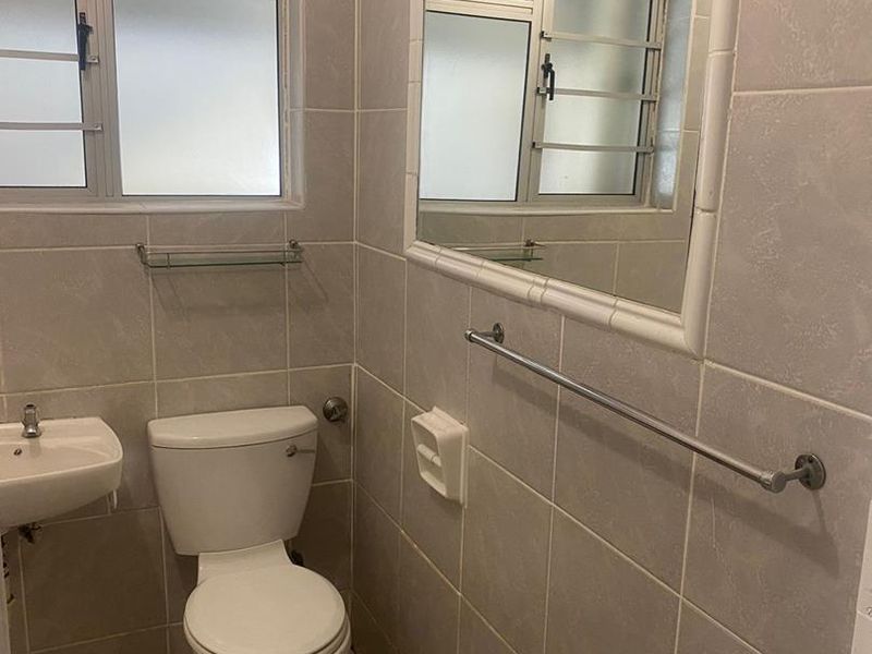 A functional bathroom featuring tiled walls and flooring, a wall-mounted basin, toilet, and a framed mirror with natural light from a frosted window.