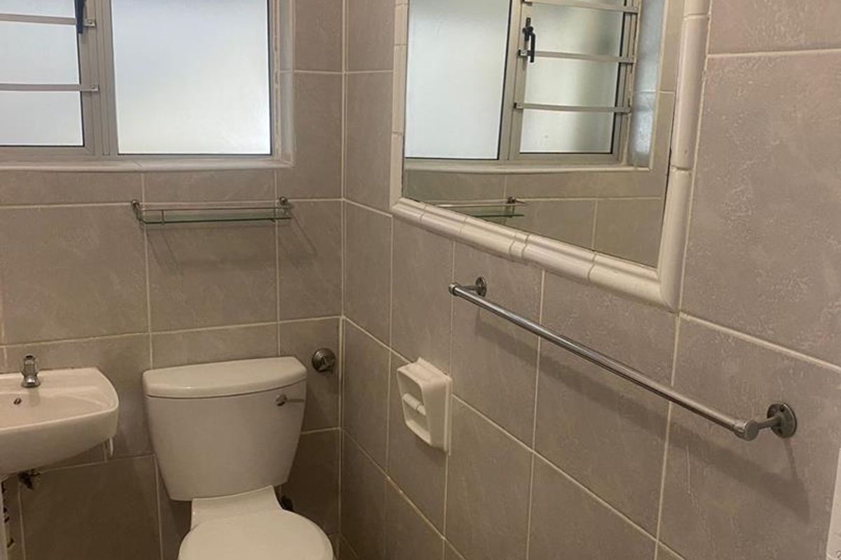 A functional bathroom featuring tiled walls and flooring, a wall-mounted basin, toilet, and a framed mirror with natural light from a frosted window.