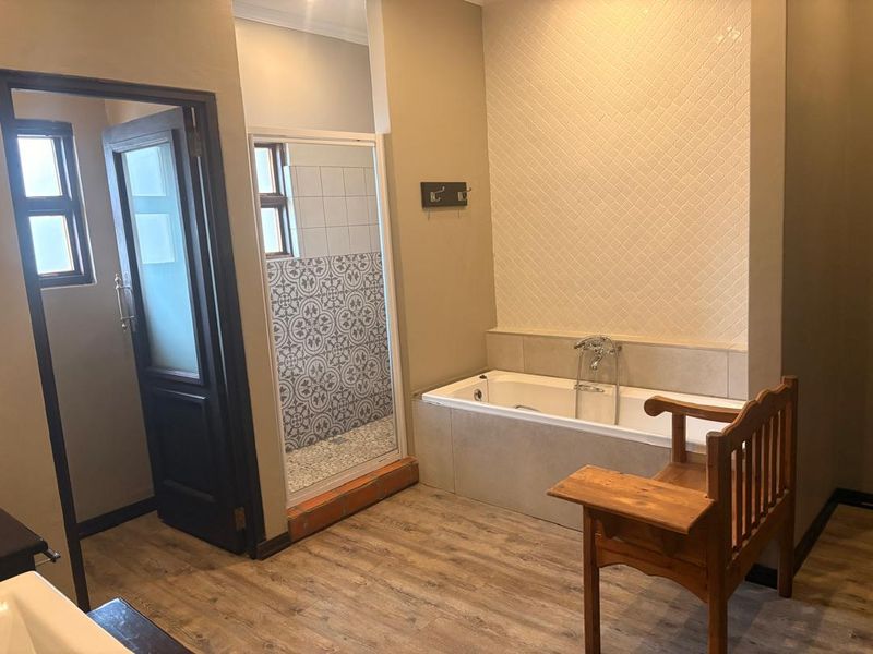A well-maintained bathroom featuring a built-in bathtub, a separate shower enclosure with decorative tiling, and modern laminate flooring.