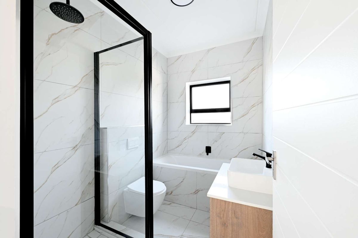 Modern bathroom featuring a walk-in shower with black-framed glass, a built-in bathtub, wall-mounted toilet, and a vanity with a countertop basin.
