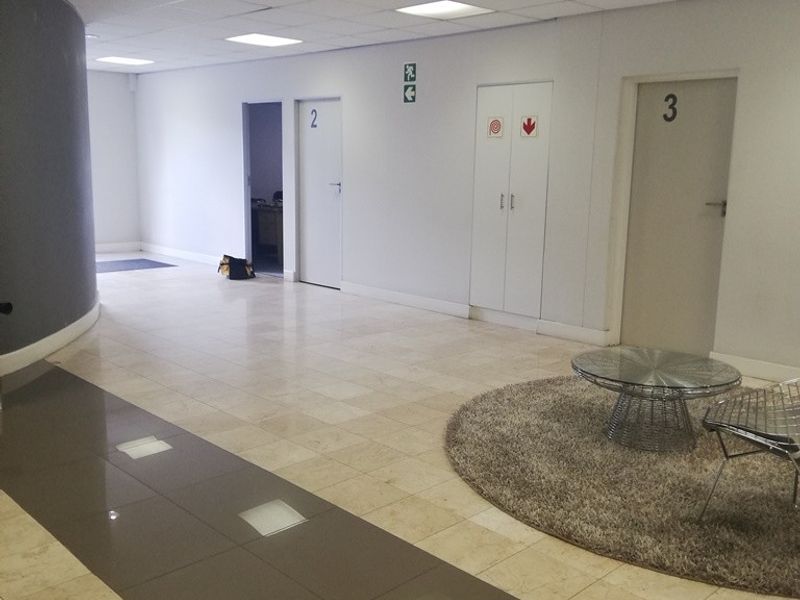 A professional office hallway featuring tiled flooring, a suspended ceiling with recessed lighting, and multiple numbered office doors.