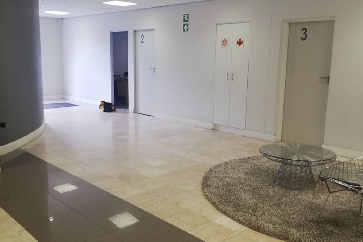 A professional office hallway featuring tiled flooring, a suspended ceiling with recessed lighting, and multiple numbered office doors.