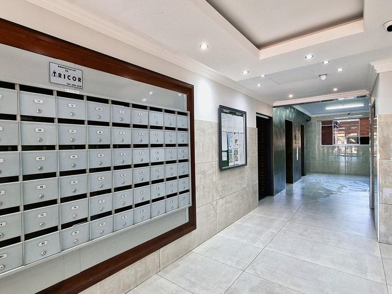 A clean and well-maintained apartment building entrance lobby featuring a large bank of built-in mailboxes, tiled flooring, and modern recessed ceiling lighting.