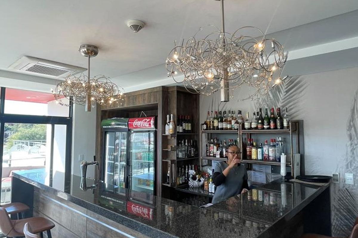A well-appointed bar area featuring a granite-topped counter, integrated shelving, and modern decorative pendant lighting, suitable for hospitality or entertainment use.