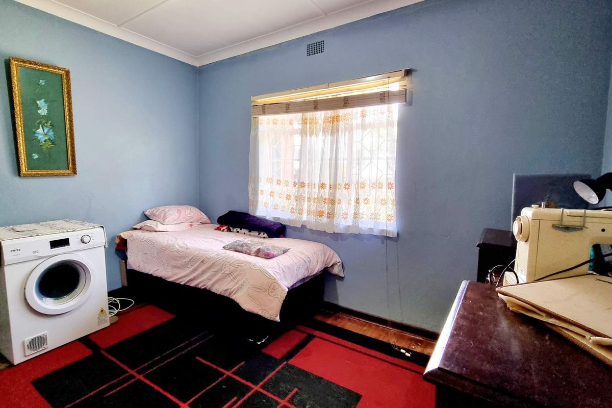 A bedroom featuring blue walls, a window with blinds, and a ceiling vent. The space is currently utilized for laundry and sewing activities.