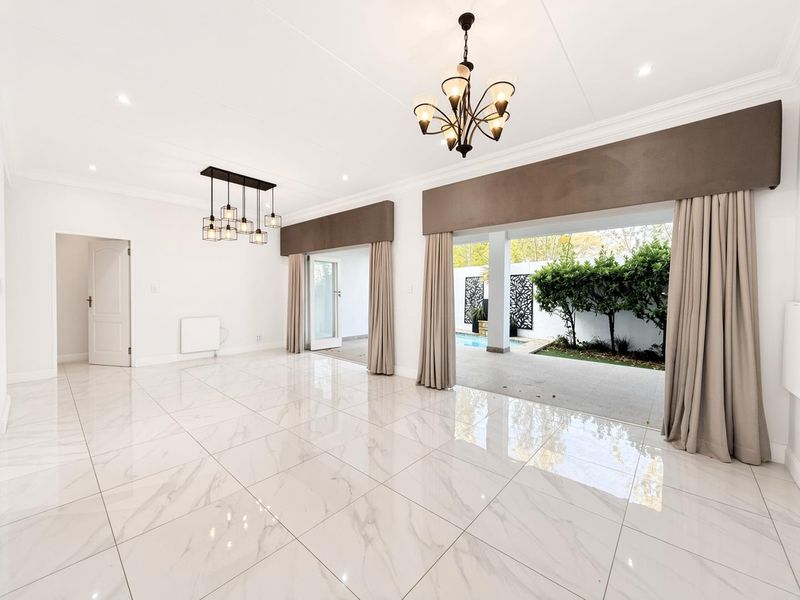 Spacious, light-filled living area featuring polished marble-look floor tiles, elegant chandeliers, and seamless flow to the outdoor patio and pool area.