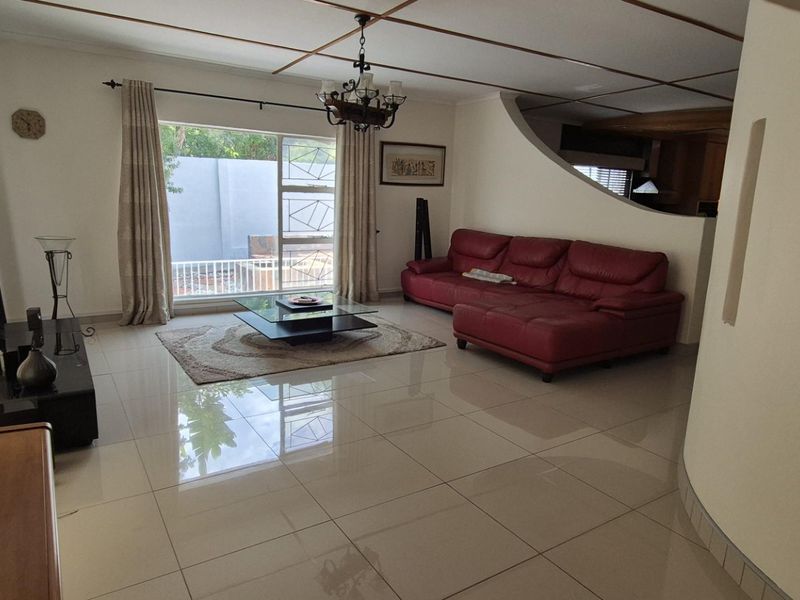Spacious living room featuring polished tiled flooring, decorative ceiling beams, and a unique curved partition wall with built-in niches, leading to an outdoor area.