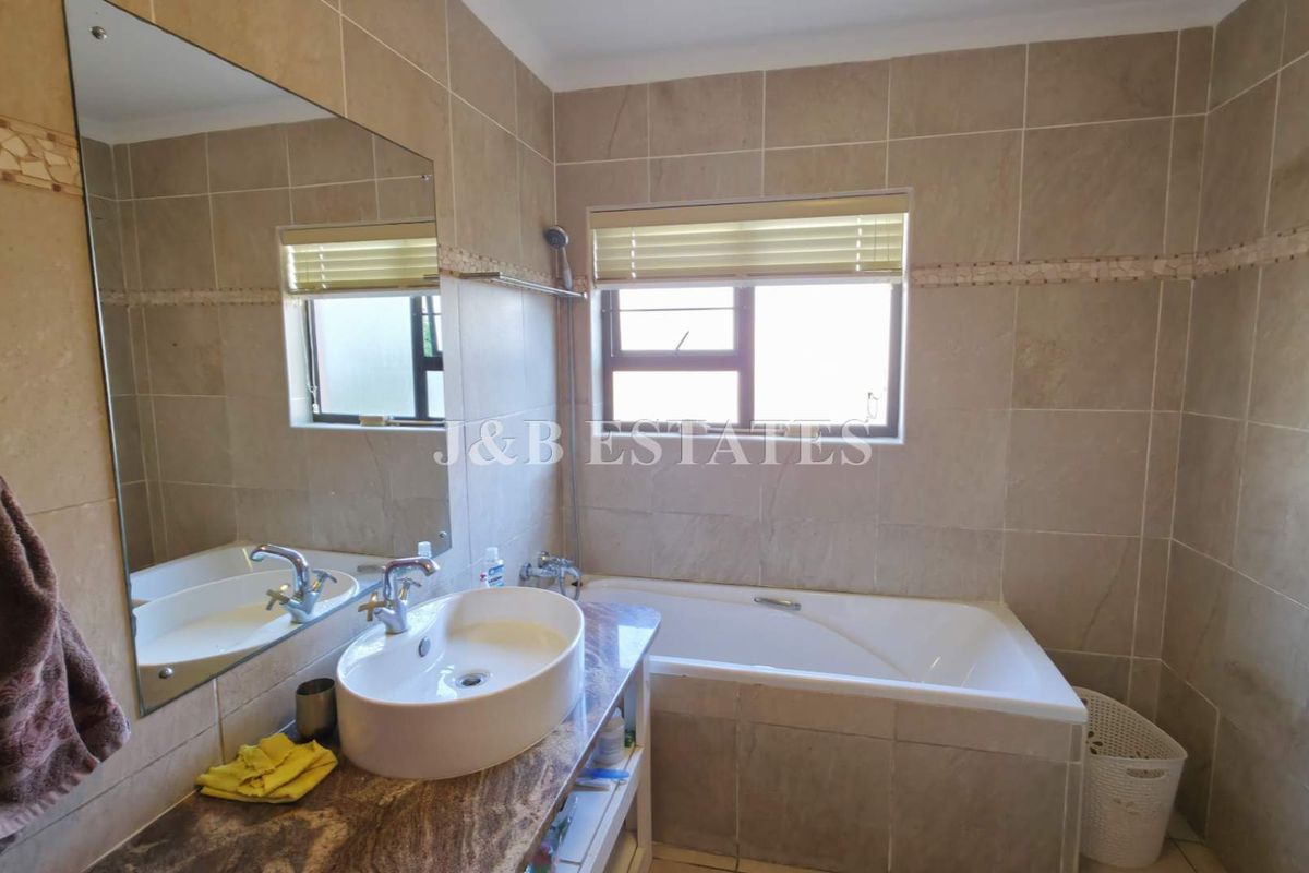 A well-maintained bathroom featuring a built-in bathtub, a modern vessel sink vanity, and floor-to-ceiling neutral wall tiling.
