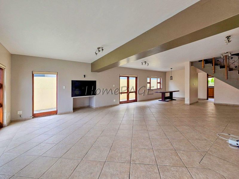 Spacious open-plan living area featuring neutral tiled flooring, a built-in television recess, and a staircase with decorative wrought iron railings.