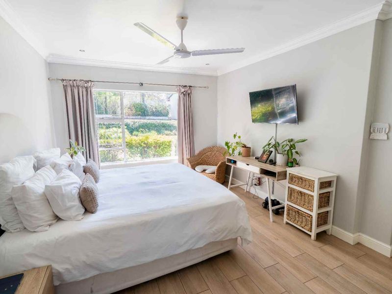 A bright and well-maintained bedroom featuring wood-look tile flooring, crown molding, and a ceiling fan, with large windows providing natural light.