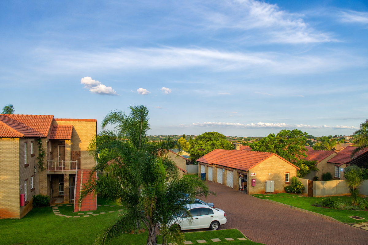 An elevated view of a townhouse complex featuring brick facades, terracotta tiled roofs, paved driveways, and a communal garden area.
