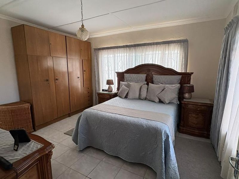 A well-maintained bedroom featuring neutral tiled flooring, a large built-in wooden wardrobe, and a window fitted with security bars.