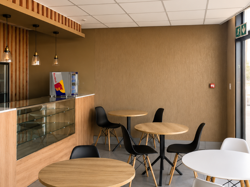 A modern retail or cafe space featuring a built-in service counter, glass display unit, suspended ceiling, and neutral tiled flooring.
