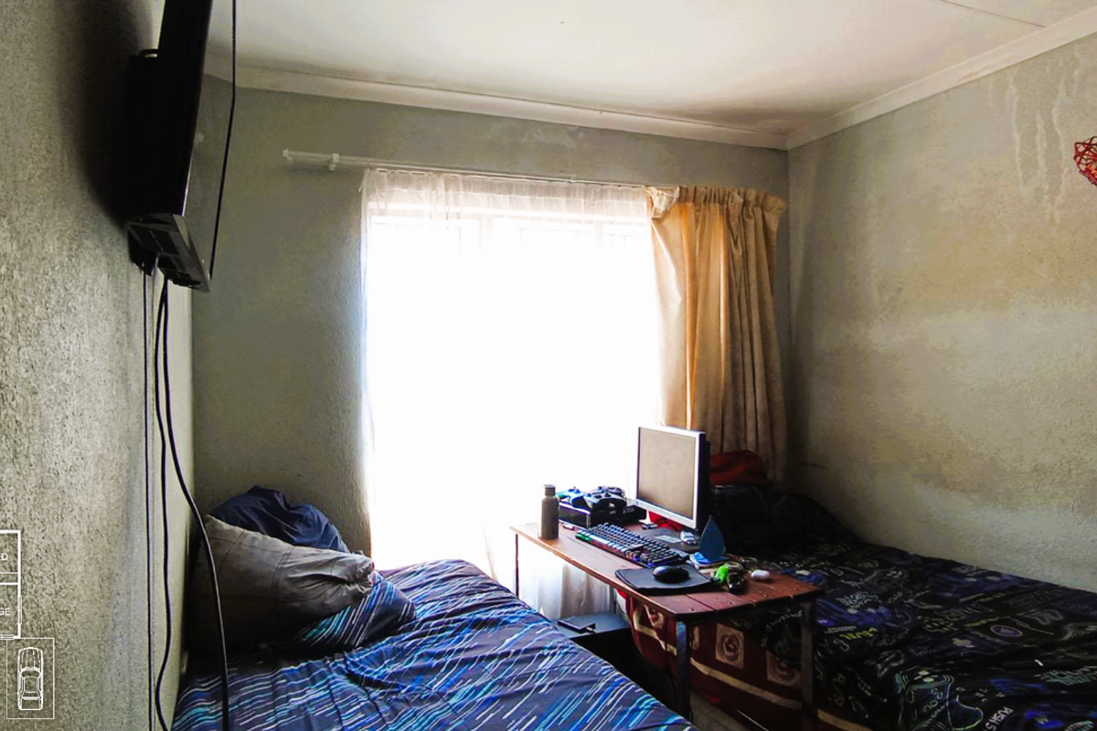 A bedroom featuring a window with curtains, showing signs of wall surface deterioration and water staining.