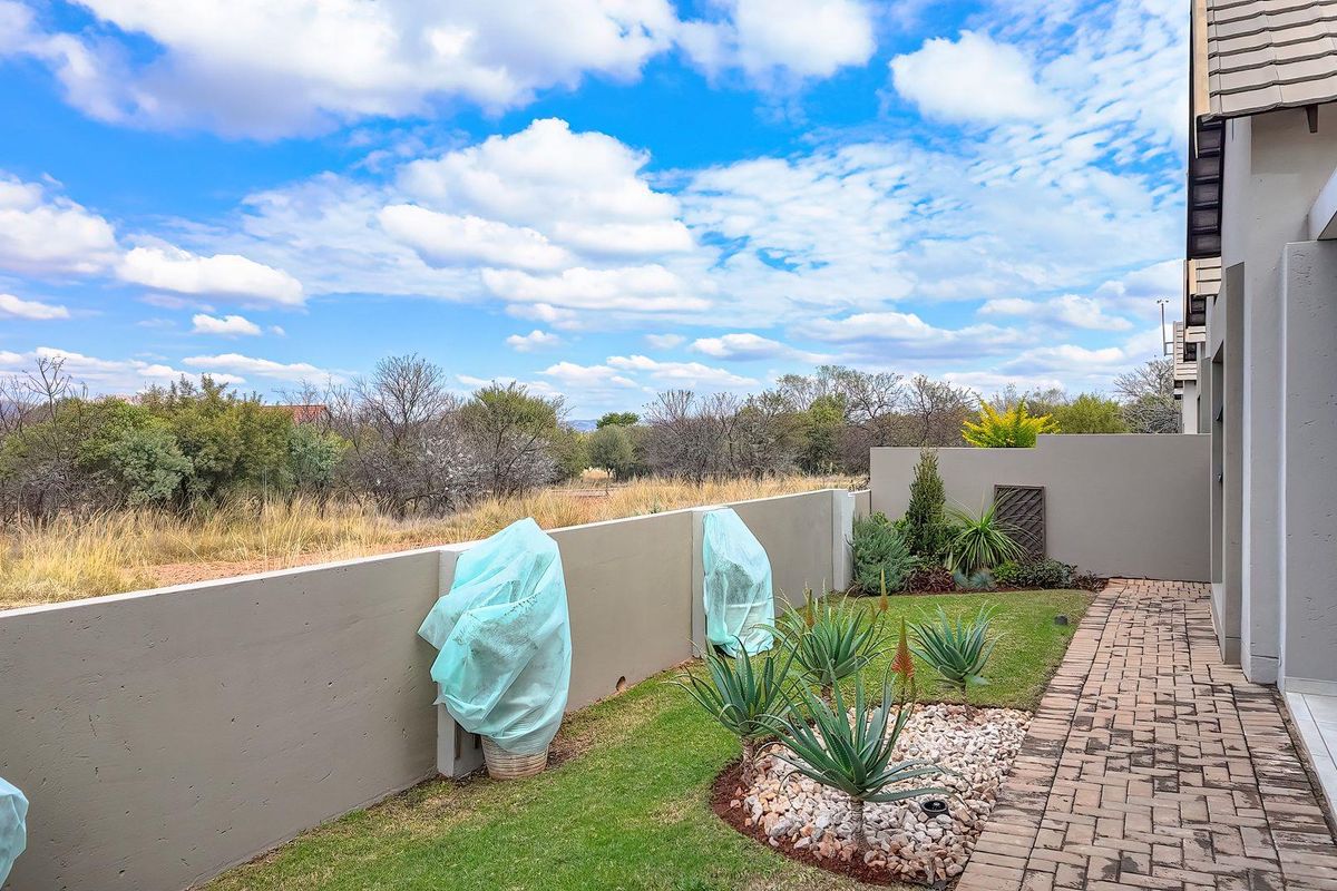A well-maintained rear garden featuring a paved walkway, landscaped lawn, and a solid boundary wall overlooking natural veld.