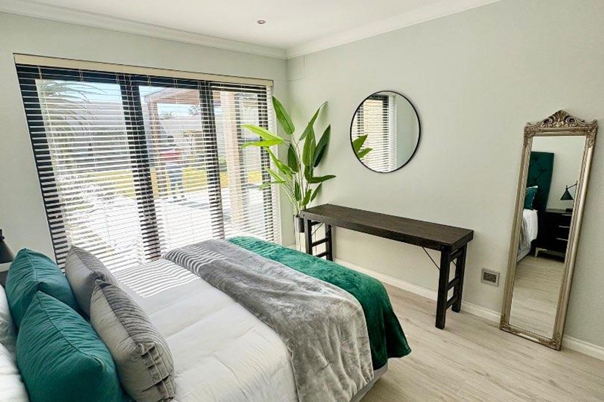 A well-maintained bedroom featuring light-toned laminate flooring, recessed downlights, and large sliding glass doors with venetian blinds providing natural light.