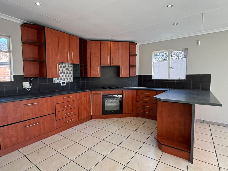 A functional kitchen featuring wood-finish cabinetry, dark countertops, built-in oven and hob, tiled backsplash, and neutral floor tiles.