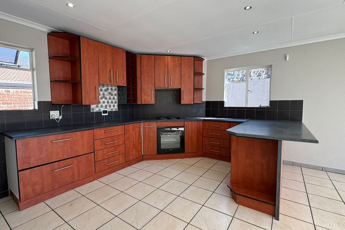 A functional kitchen featuring wood-finish cabinetry, dark countertops, built-in oven and hob, tiled backsplash, and neutral floor tiles.