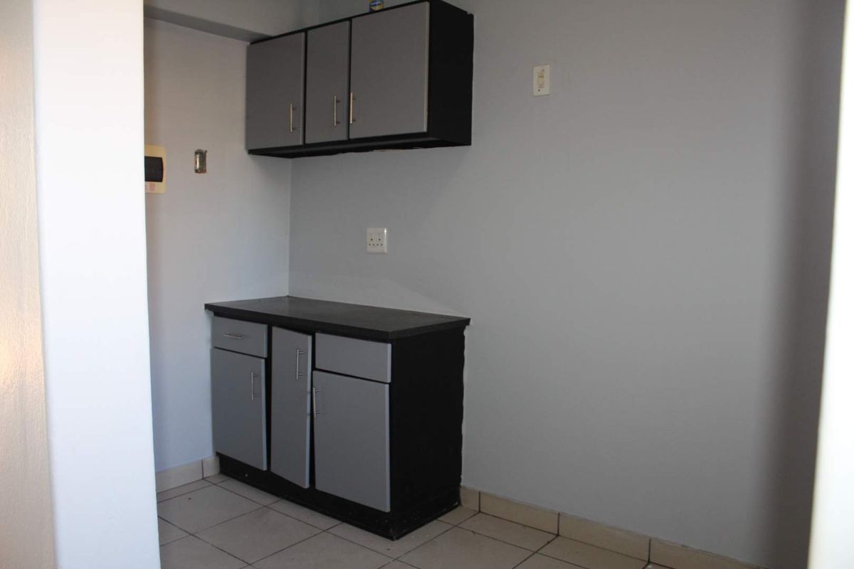 A compact kitchen area featuring built-in grey and black cabinetry with a laminate countertop and tiled flooring.