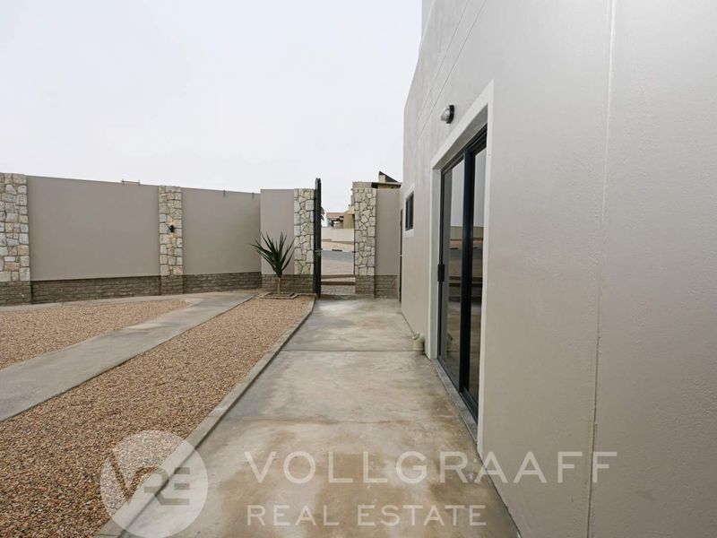 A clean rear exterior area featuring a concrete walkway, gravel landscaping, and a modern sliding glass door access point.