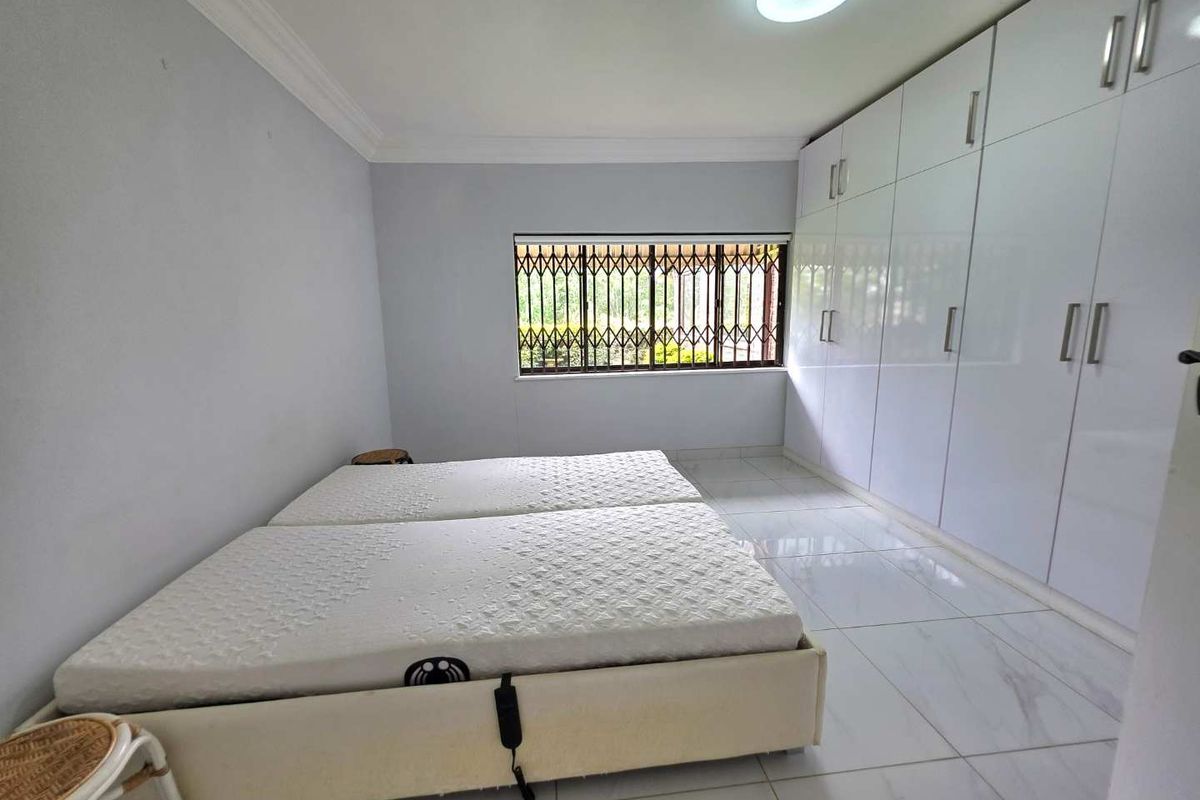 A bright bedroom featuring large built-in white cabinetry, tiled flooring, and a window fitted with security bars.