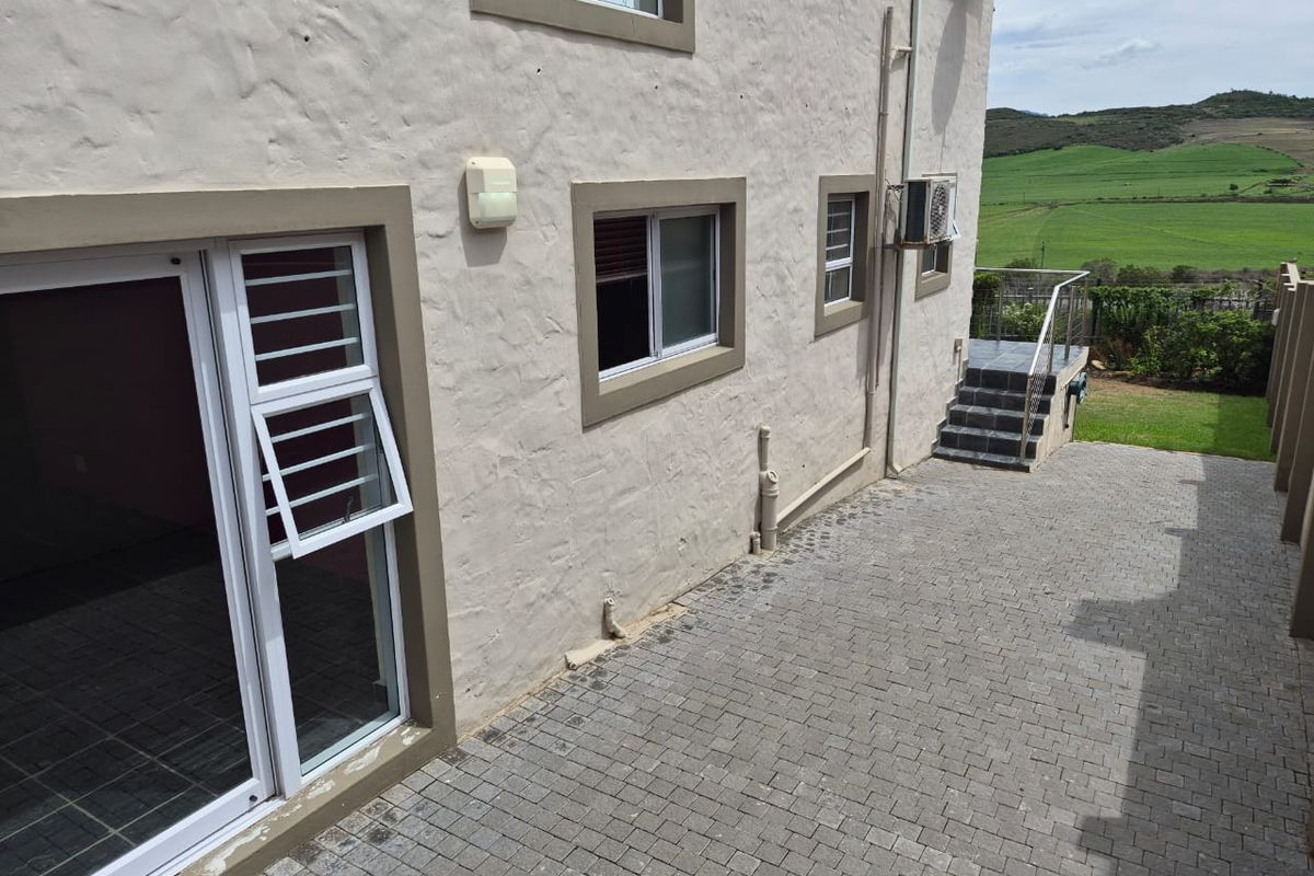 Rear exterior view of the property featuring paved courtyard, sliding glass doors, and external staircase leading to the garden area.