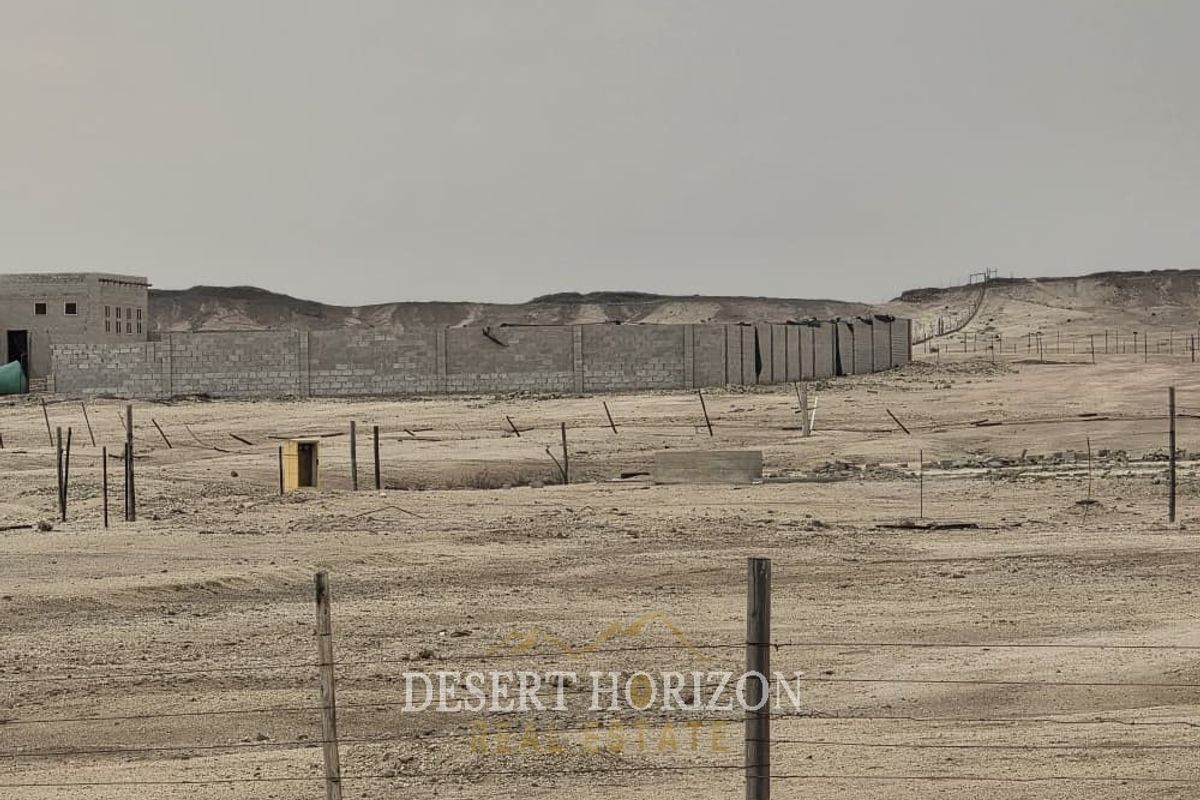 A view of a large, undeveloped small holding plot featuring a perimeter wall and wire fencing in a desert landscape.