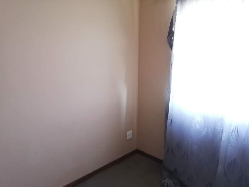 A simple, empty bedroom corner featuring neutral walls, skirting boards, and a window with curtains.