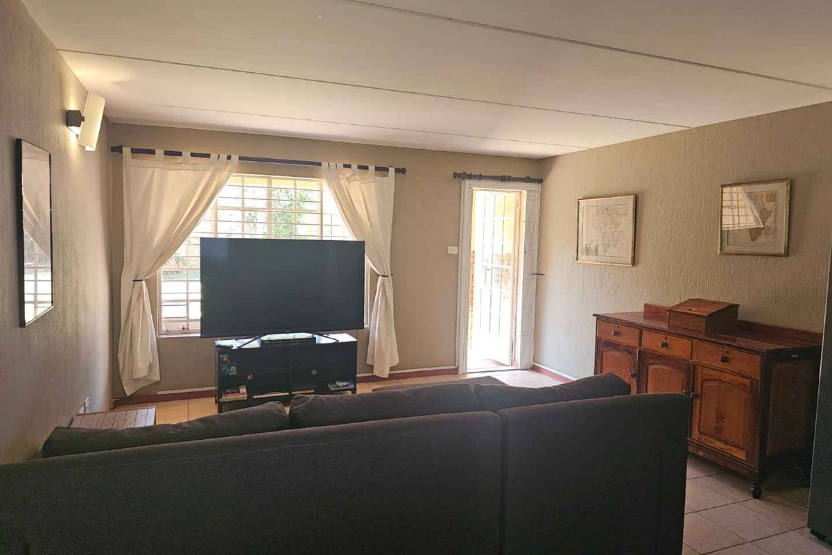 A comfortable living room featuring tiled flooring, natural light from the window, and direct access to an outdoor area through a security gate.