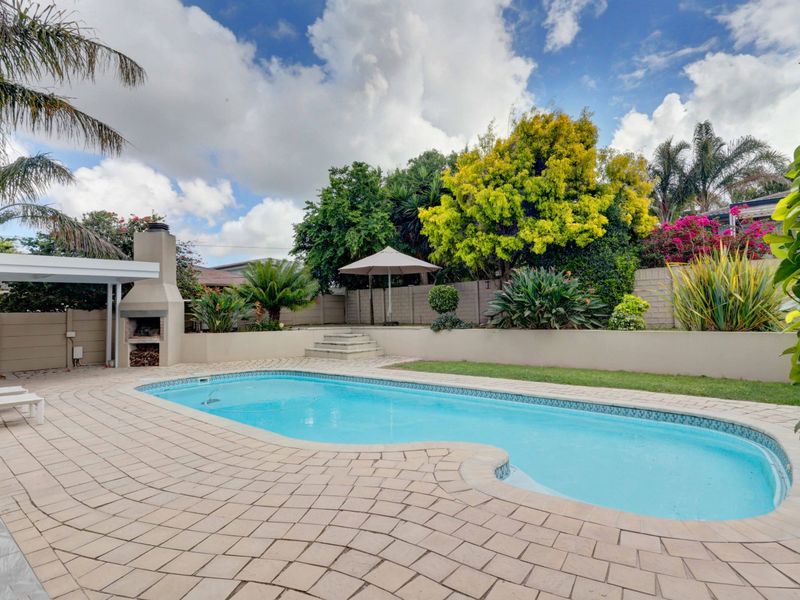 Outdoor entertainment area featuring a swimming pool, paved patio, and a built-in braai, set within a landscaped garden with perimeter walling.