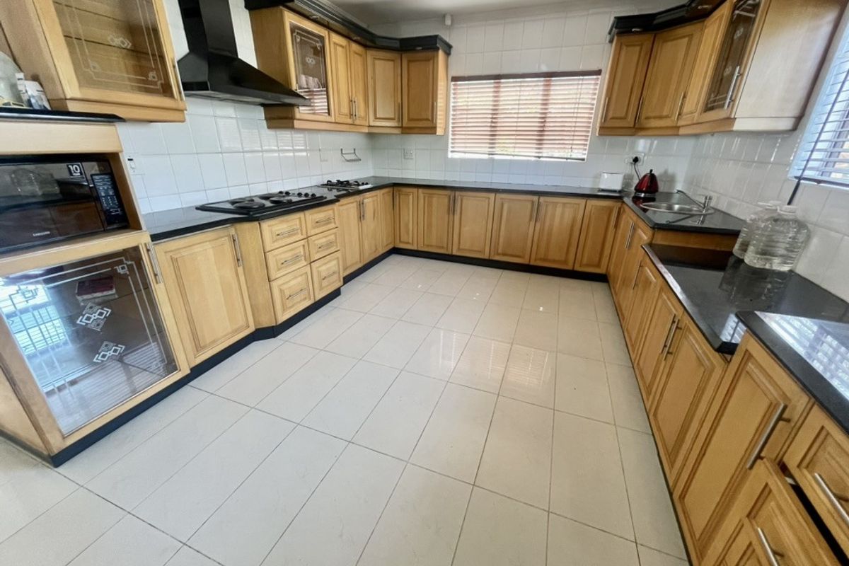Spacious kitchen featuring extensive wooden cabinetry, granite countertops, a gas hob with extractor, and tiled flooring throughout.