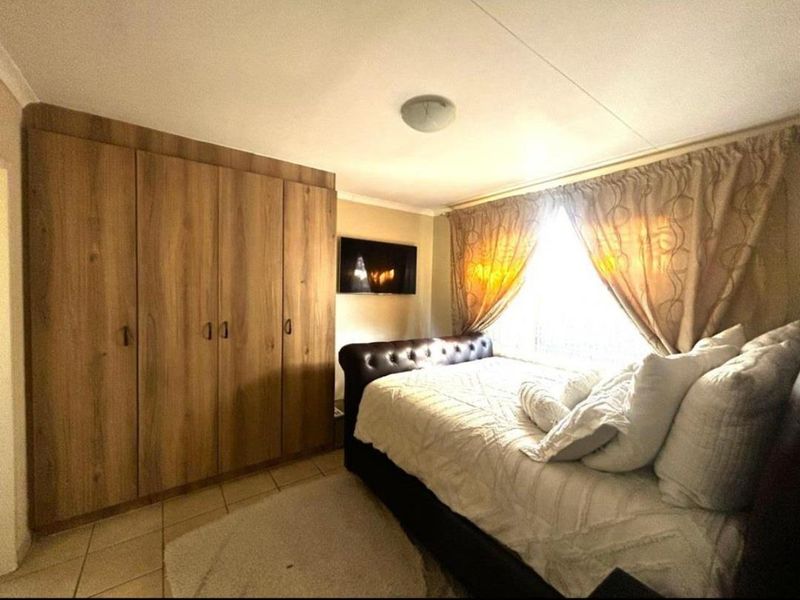 A bedroom featuring built-in wooden cupboards, tiled flooring, and a ceiling light fixture, providing a functional and comfortable living space.