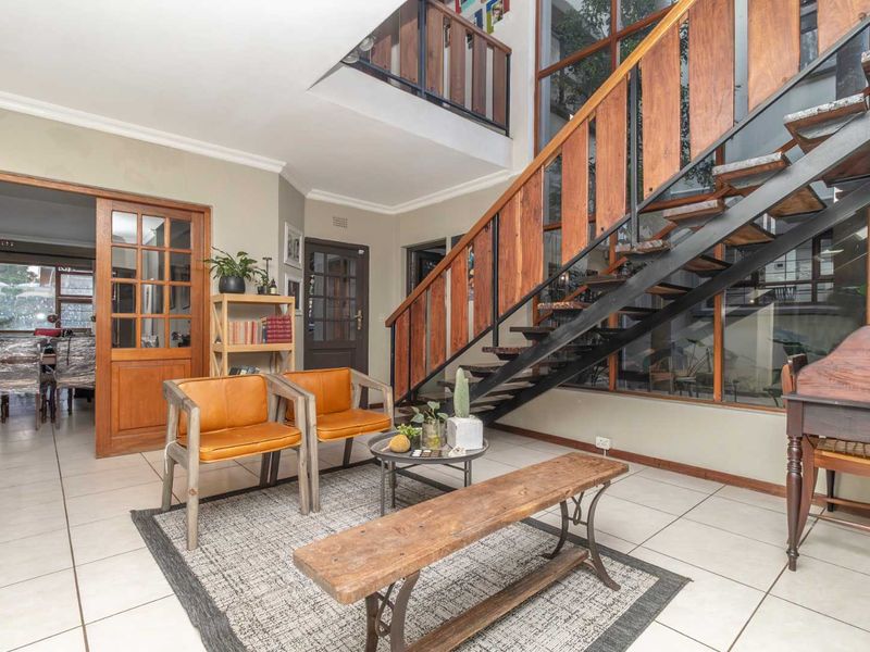 Spacious living area featuring a striking open-tread timber staircase, tiled flooring, and double-volume ceilings with large windows providing natural light.