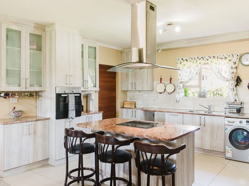 A well-appointed kitchen featuring light wood-grain cabinetry, stone countertops, a central island with a built-in hob, and integrated stainless steel appliances.